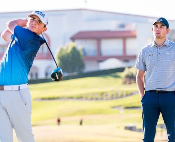 Young golfer strikes ball watched by coach