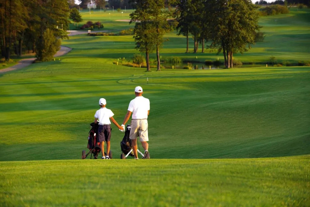 man with his son golfers walking on perfect golf course at summer evening