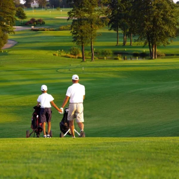 man with his son golfers walking on perfect golf course at summer evening