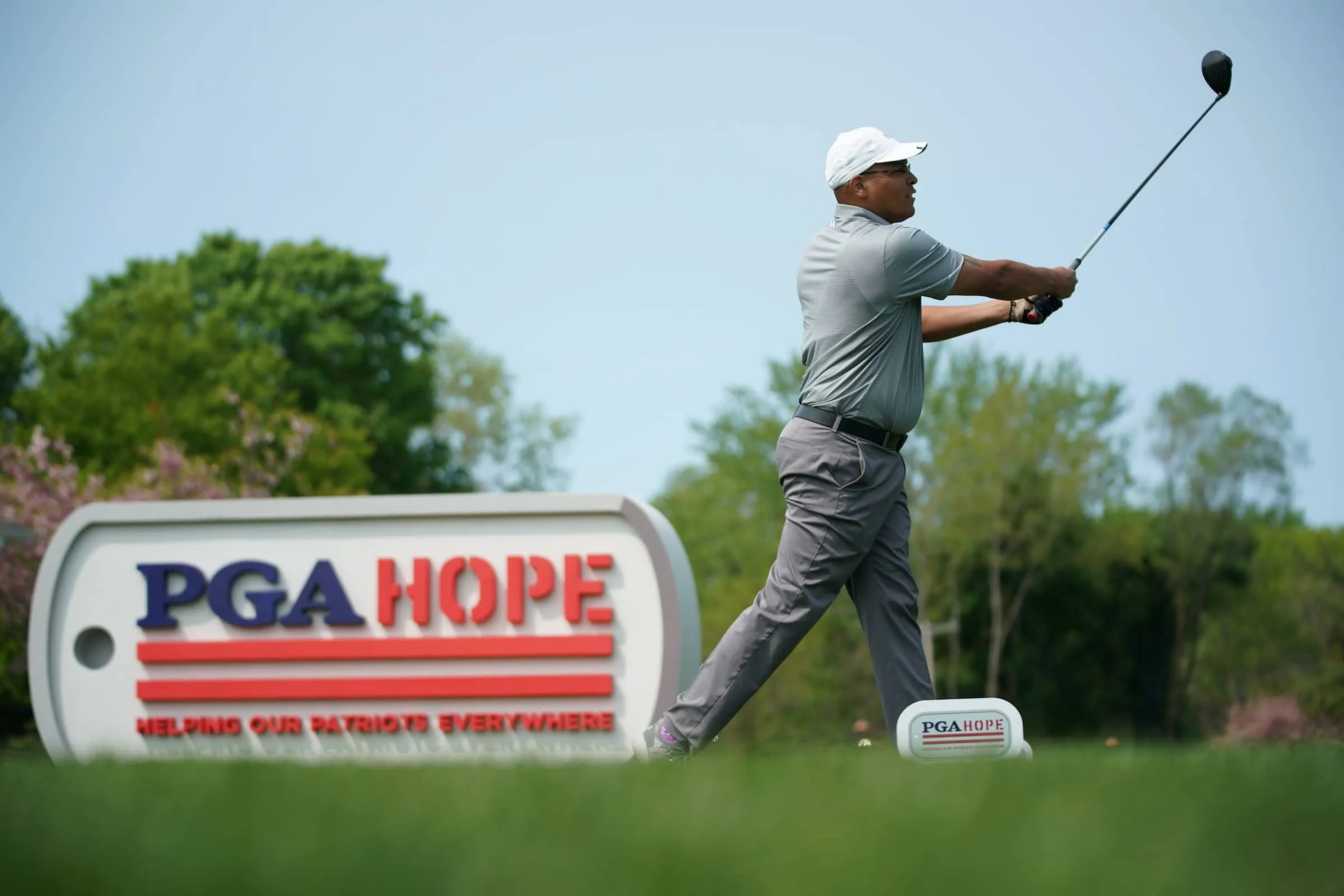 Golfer tees off next to PGA HOPE advertising board