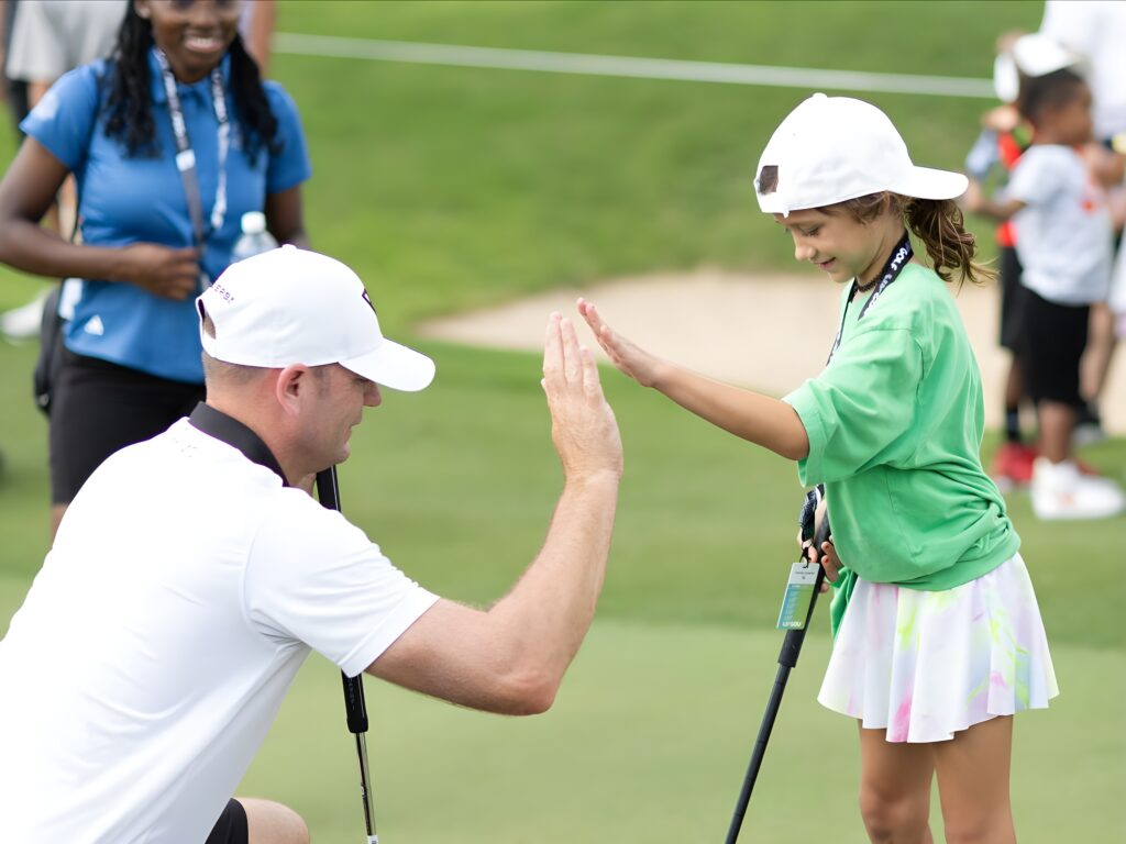 Brendan Steele of HyFlyers GC is seen with a participant at the Potential Unleashed activation before the start of LIV Golf Dallas at Maridoe Golf Club