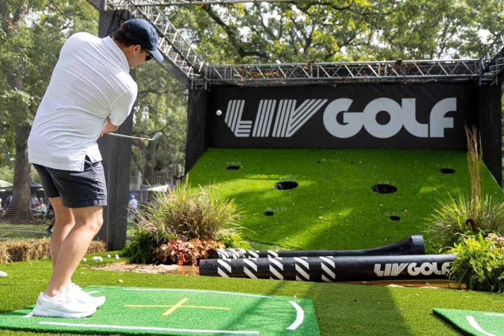 Young man hits a golf ball into LIV Golf signage